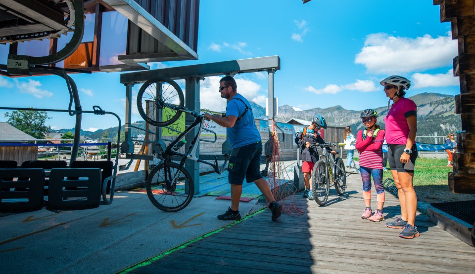 Embarquement d'une jeune fille et de sa maman au télésiège de la Logère pendant qu'un agent charge leurs vélos.